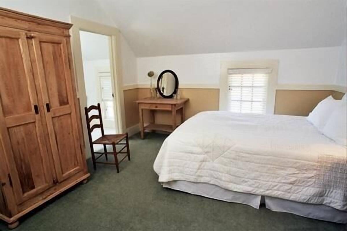 A bedroom with a large bed, a wooden wardrobe, a desk with a mirror, and a chair.