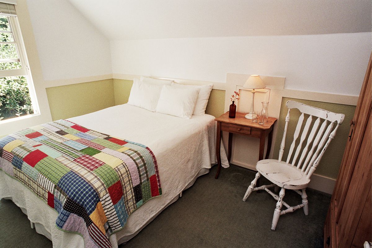 Een slaapkamer met een bed, een stoel, een nachtkastje en een raam.