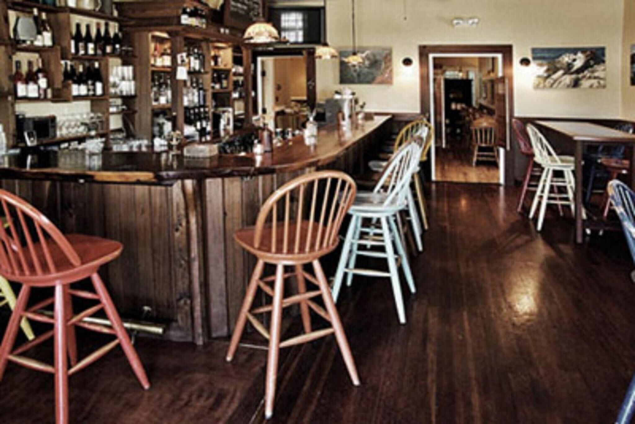 A bar area with wooden bar stools and a variety of bottles on shelves.
