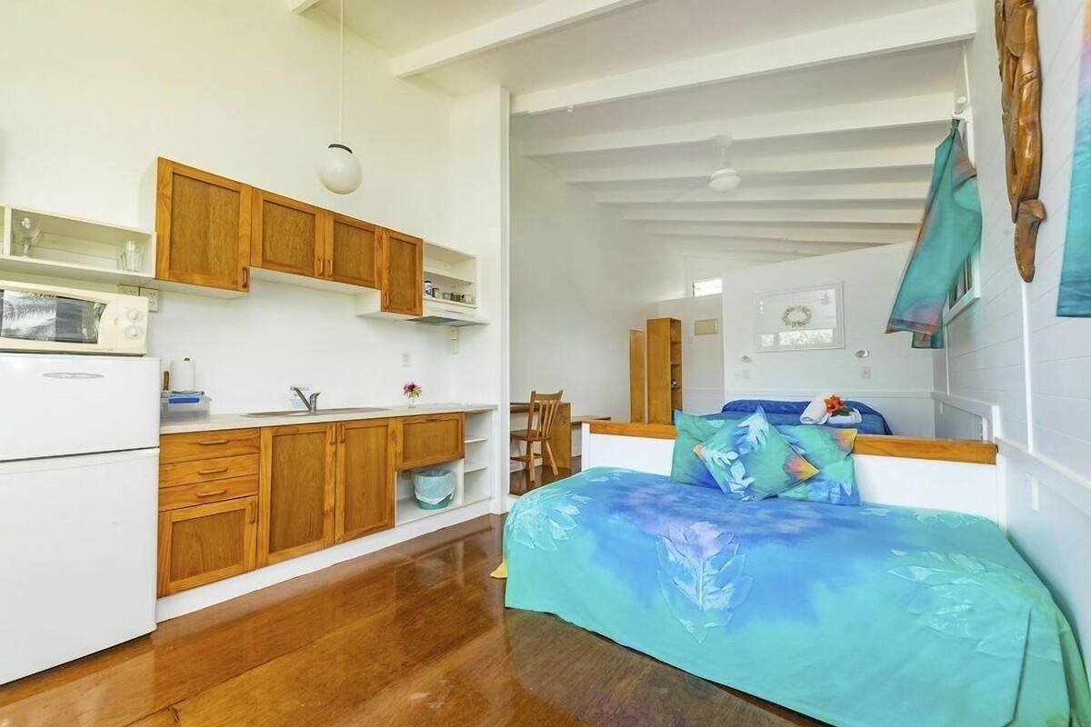 Habitación compacta con kitchenette, cama con colcha estampada y techo de madera.