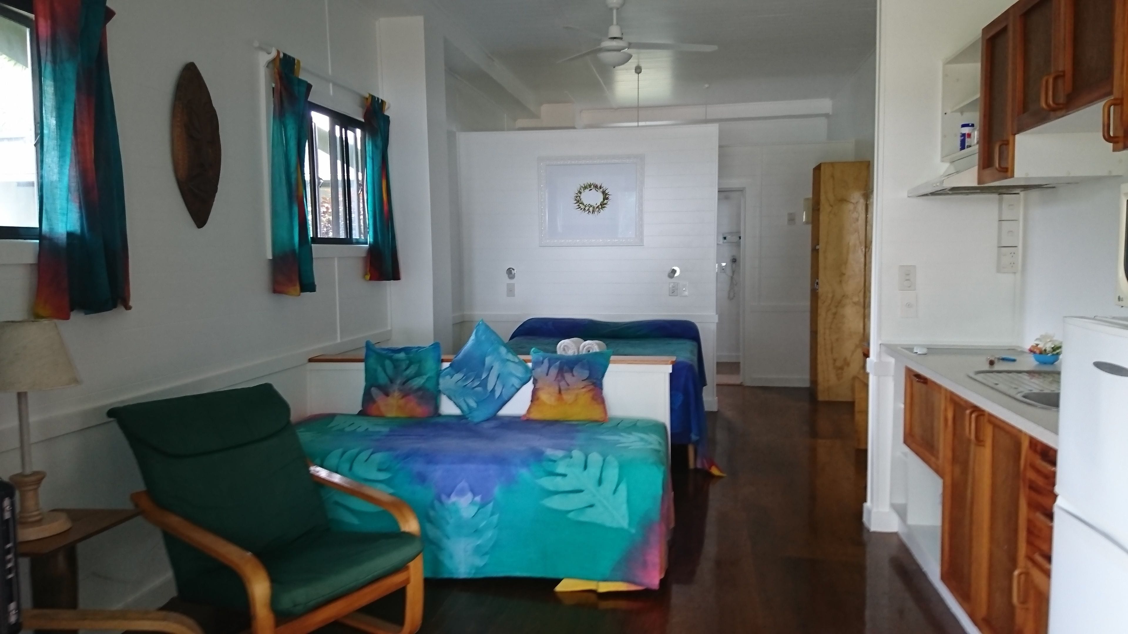Quarto com cama, cadeira, área de cozinha e porta que dá para outro cômodo.
