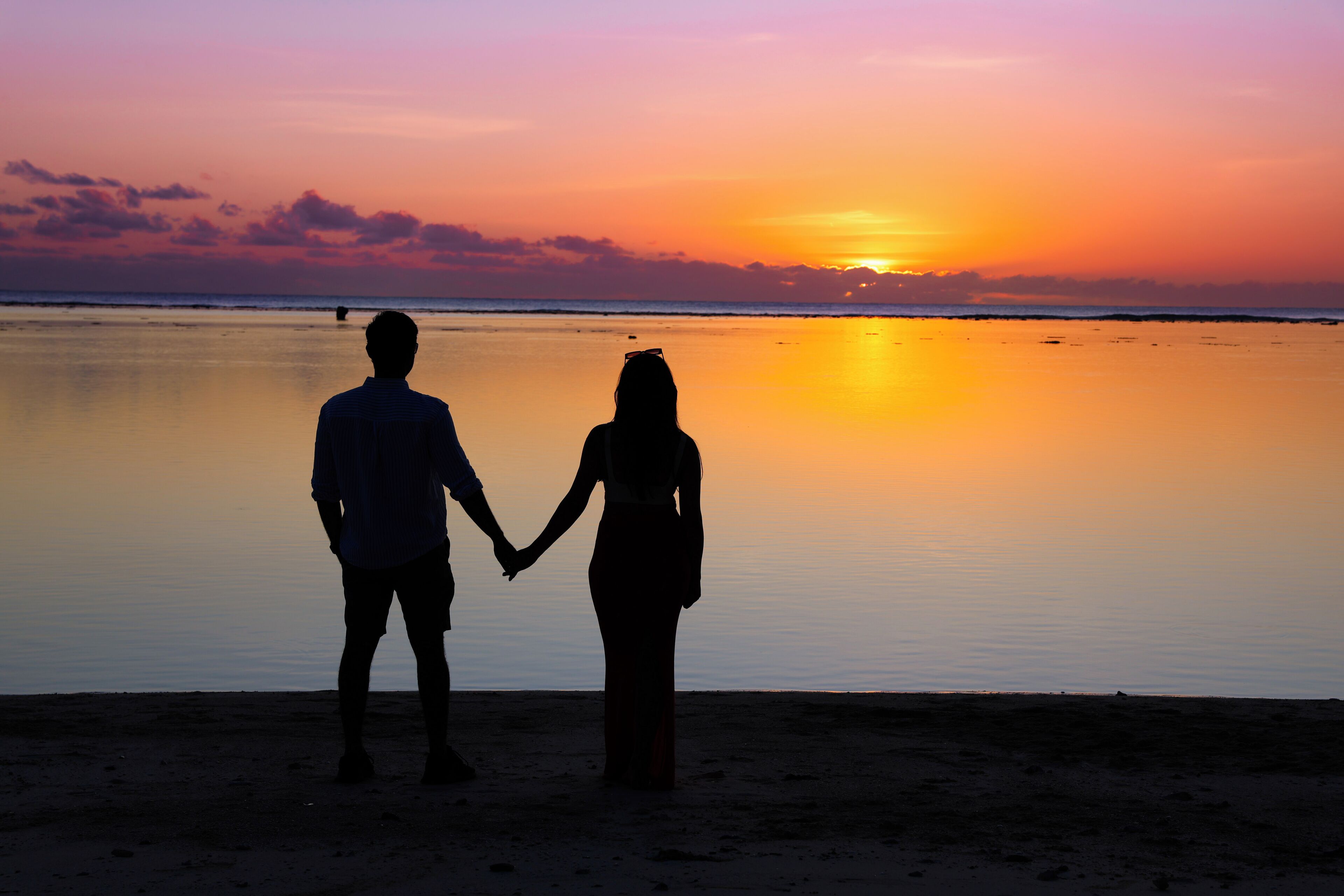 Due persone che si tengono per mano su una spiaggia al tramonto.