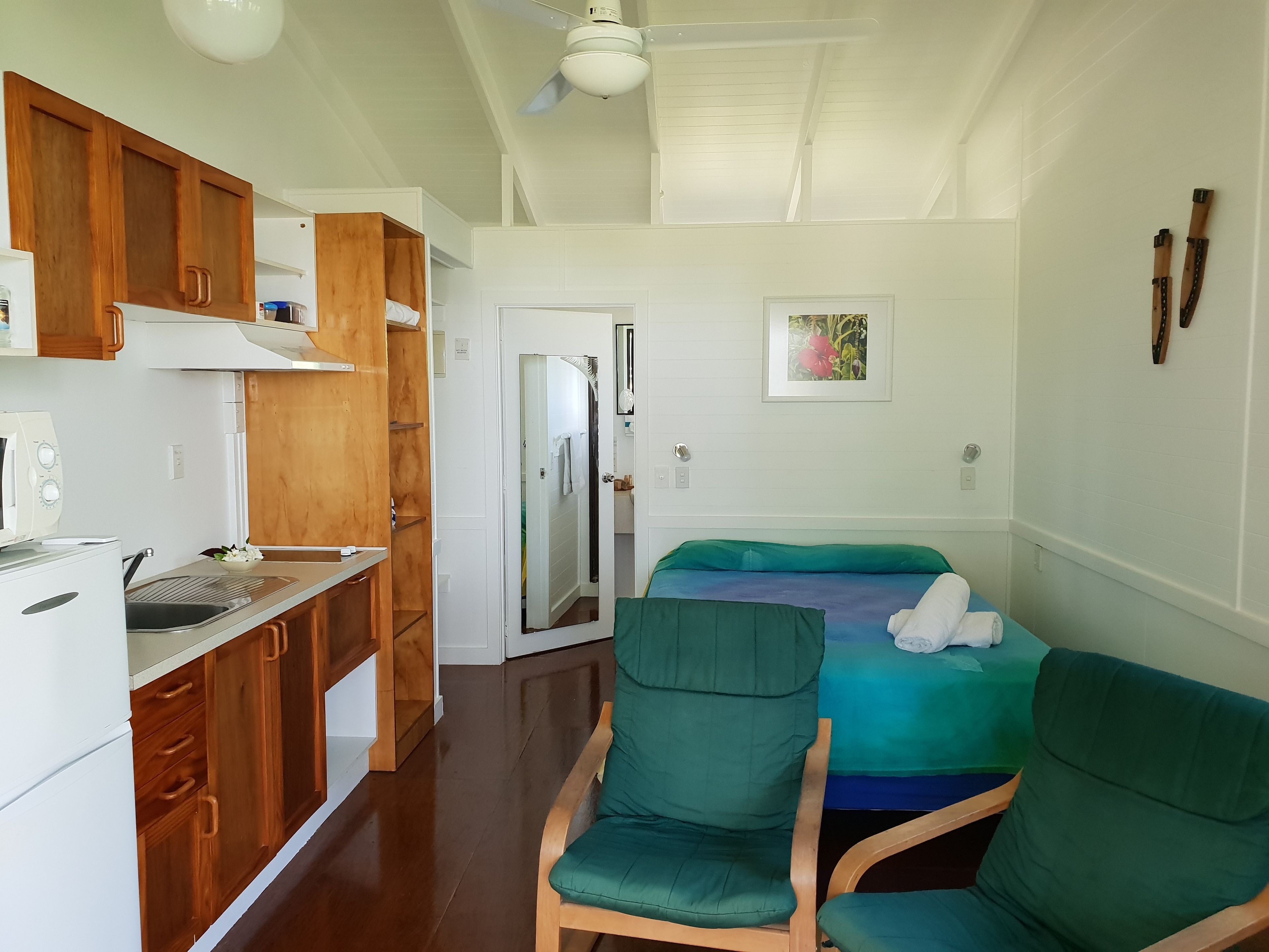 A compact room with a kitchenette, a bed with green bedding, and a ceiling fan.