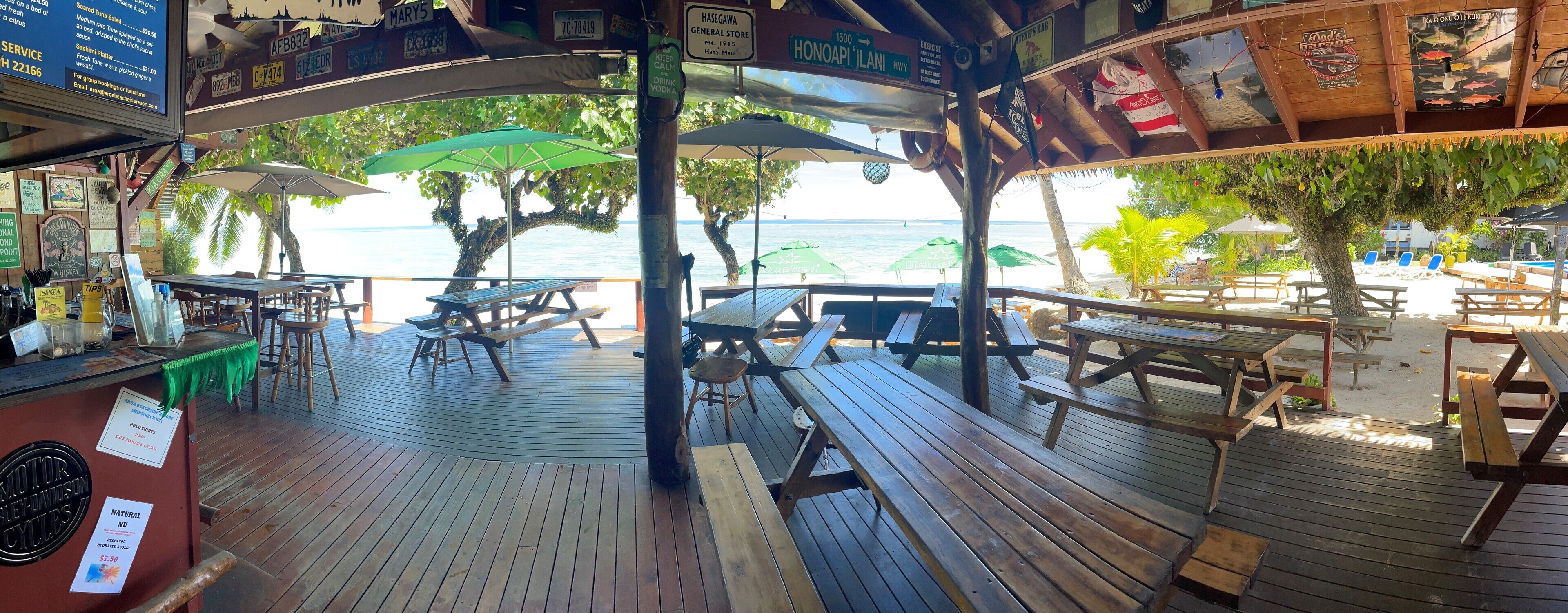 A wooden deck with picnic tables and umbrellas overlooking a beach.