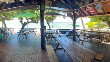 A wooden deck with picnic tables and umbrellas overlooking a beach.