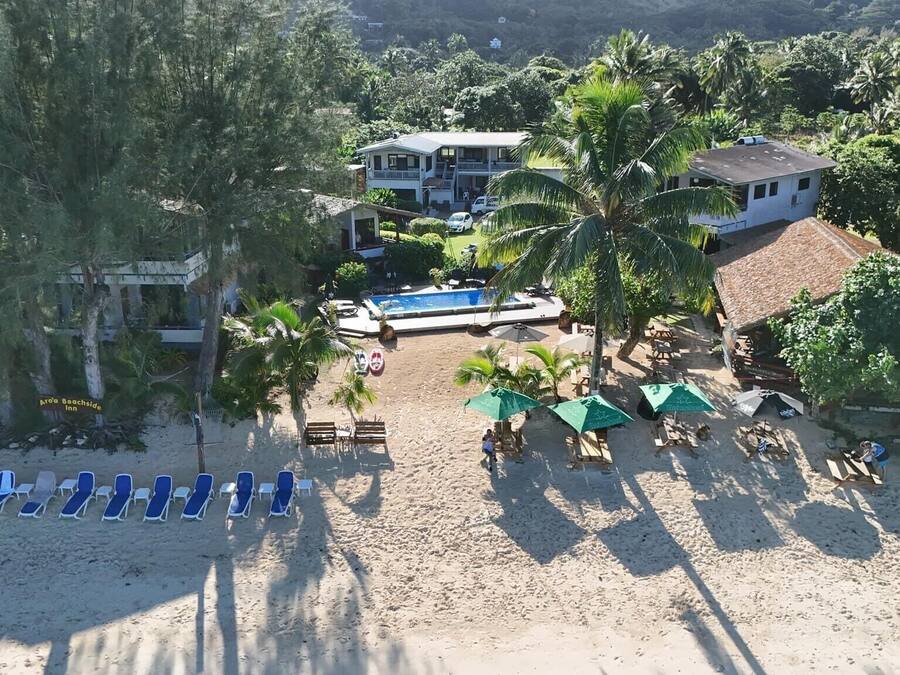 Ett semesterhotell vid stranden med en pool, solstolar och en stor byggnad med en balkong som vetter mot stranden.