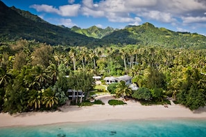 A tropical resort with a beach, lush greenery, and mountains in the background.
