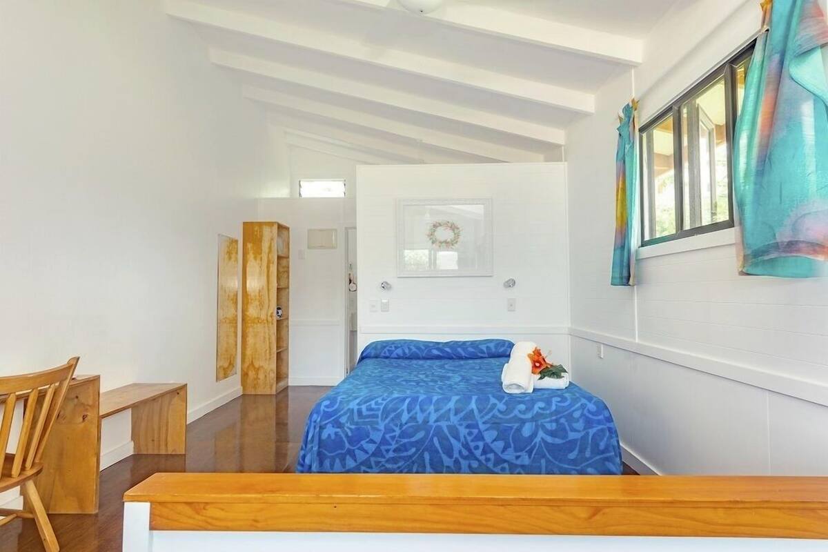 Un dormitorio con cama, un escritorio de madera, una silla, una ventana con cortinas y una puerta que da a otra habitación.