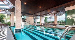 An indoor swimming pool with clear blue water, surrounded by lounge chairs and umbrellas, and a staircase leading to an upper level. - Best Western Chaweng Samui (Koh Samui)