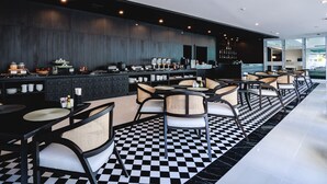 Eine moderne Bar mit Schachbrettboden, schwarzen und weißen Stühlen und einer dunklen Holzwand.