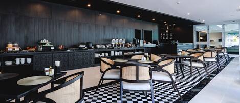 Zona de bar moderna con suelo de cuadros, sillas negras y blancas, y una pared de madera oscura.
