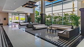 Eine großzügige Lobby mit Schachbrettmuster-Boden, moderner Sitzgelegenheiten, großen Fenstern und einer Dachkuppel.