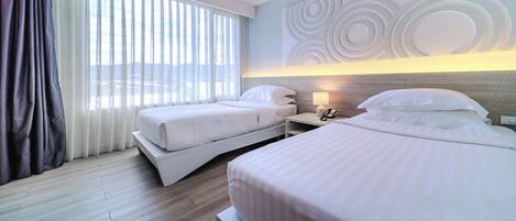 A hotel room with two beds, a window with curtains, a bedside table with a lamp, and a wall with circular patterns.