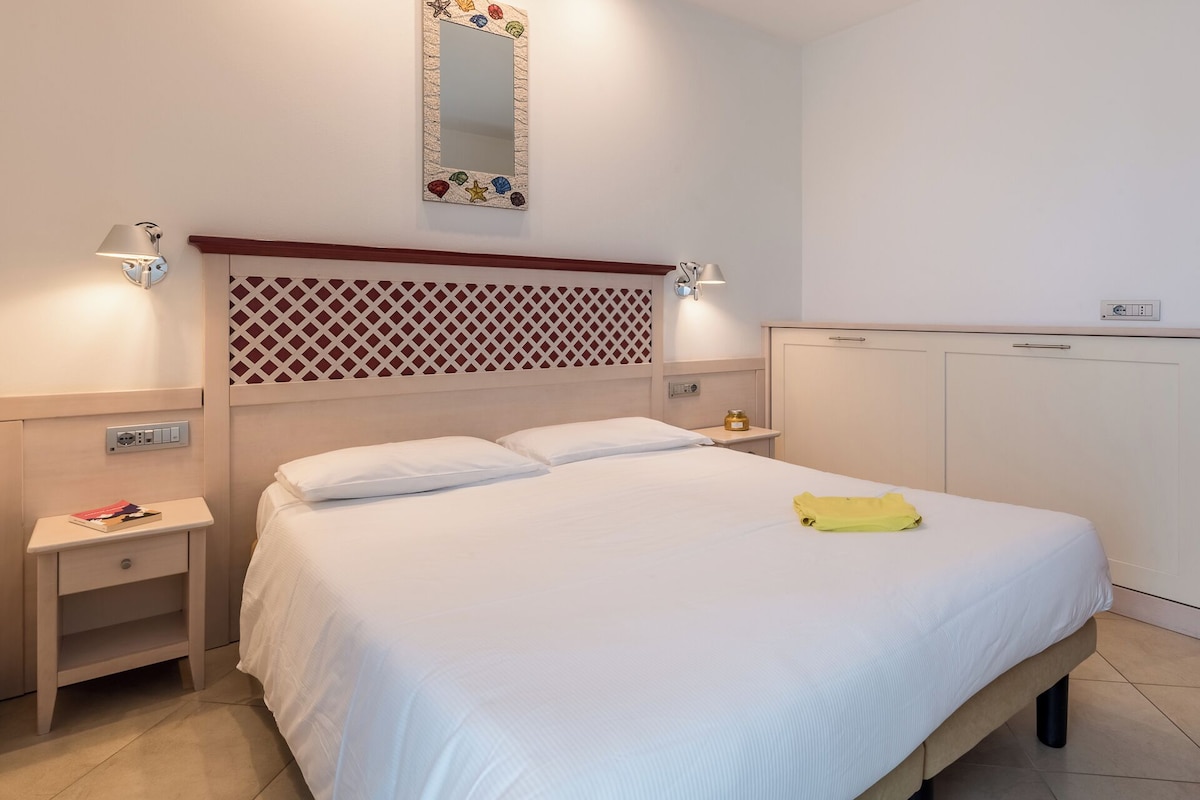 A neatly made bed with white linens, a bedside table with a book, a lamp, and a small decorative item on the nightstand.