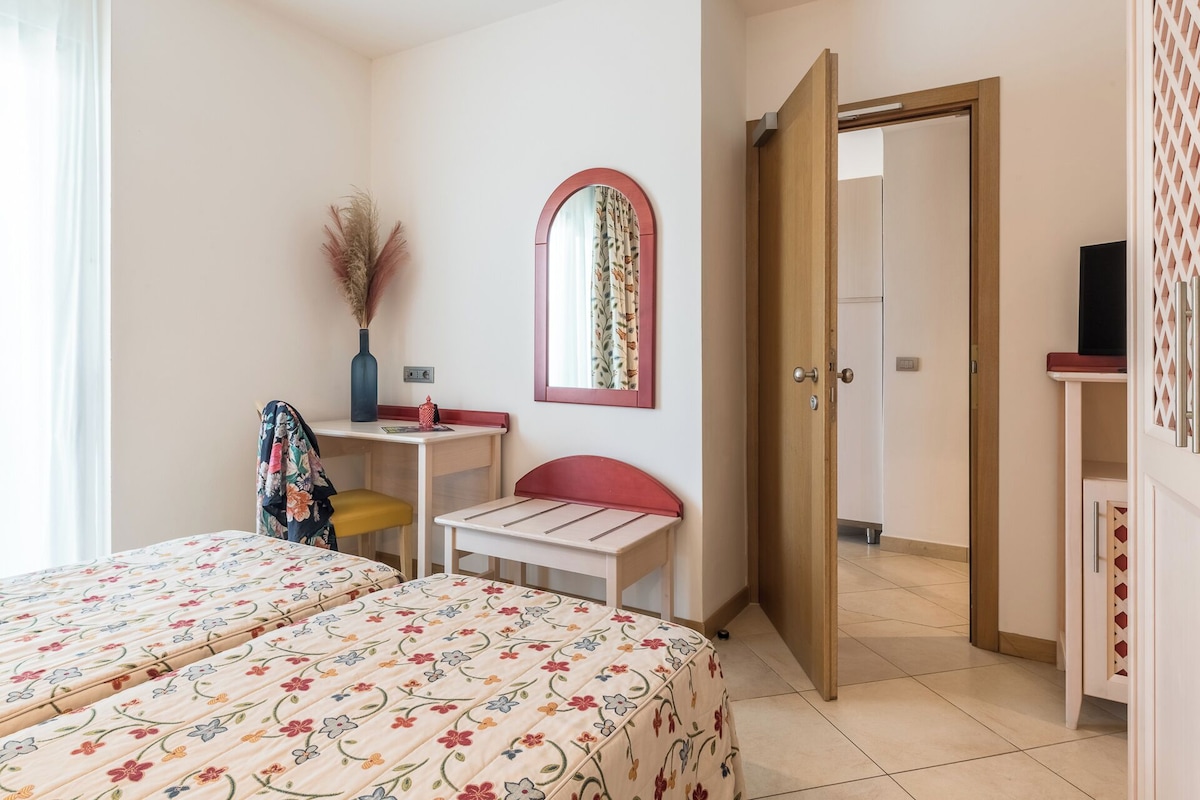 A bedroom with two beds, a desk, a chair, a mirror, and a wardrobe.