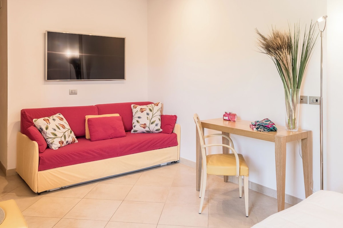 A compact living space with a red sofa, a wooden table, and a TV mounted on the wall.