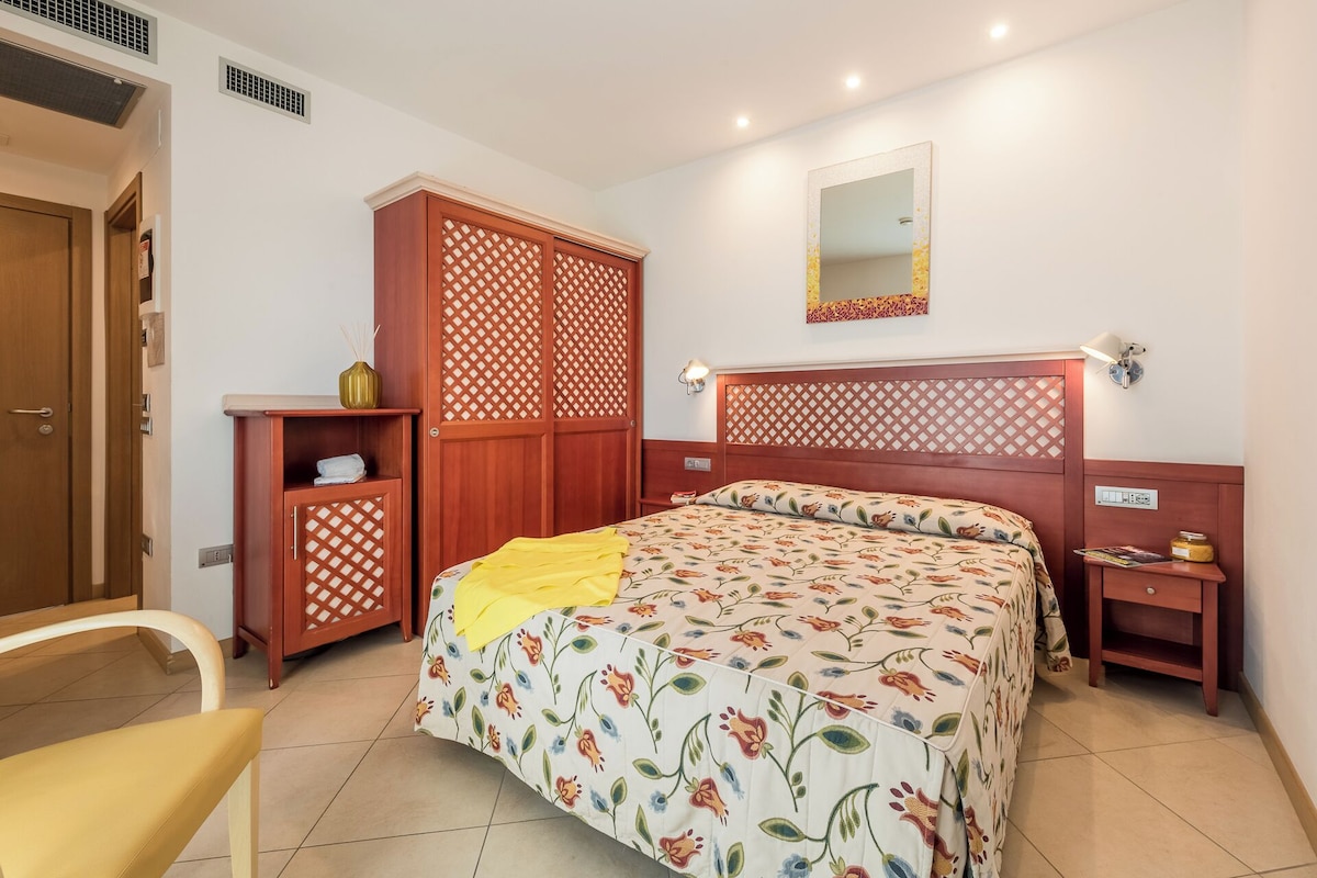 A bedroom with a bed, a wardrobe, a bedside table, a chair, and a mirror on the wall.
