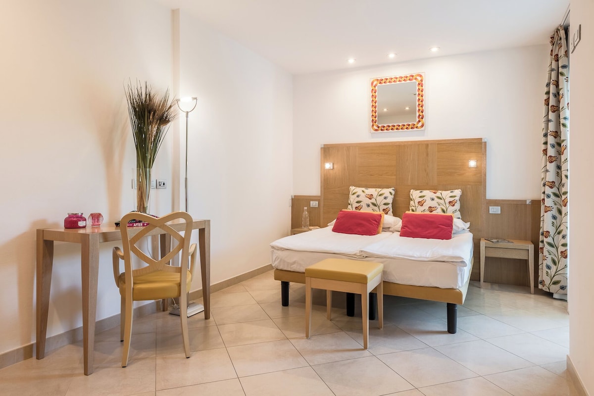 A hotel room with a bed, bedside tables, a desk, and a chair.