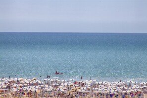 A beach with numerous umbrellas and beach chairs, a clear sky, and a calm sea.