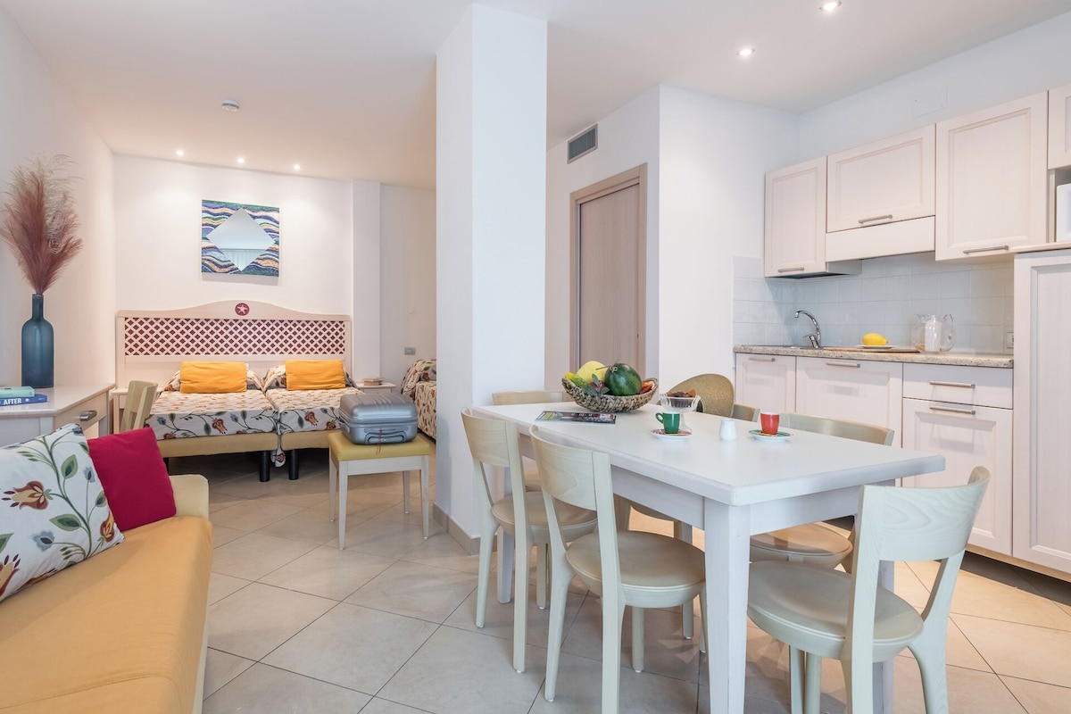 A modern, well-lit apartment with a dining area, kitchen, and a bed with a patterned headboard.