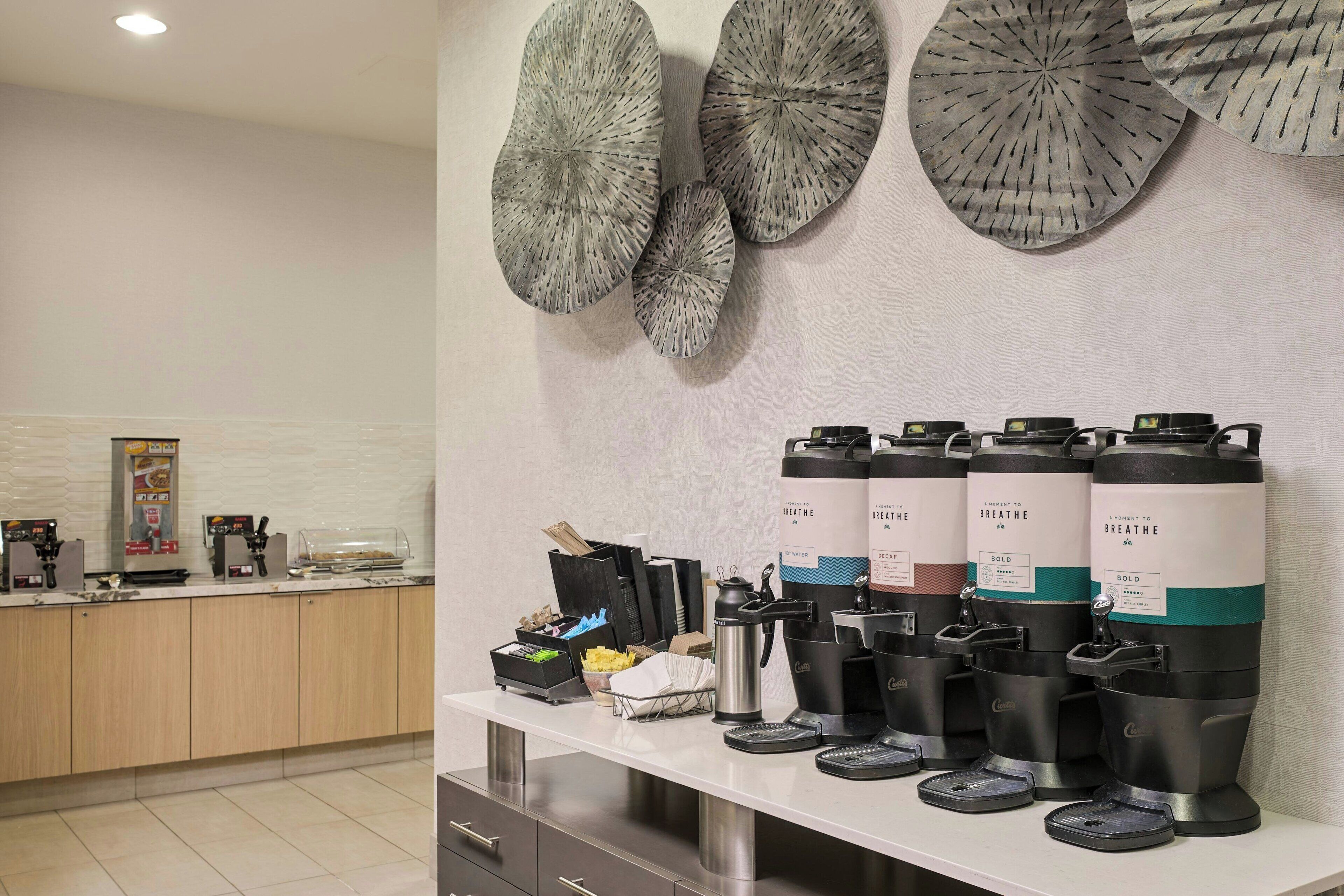 A modern coffee station with multiple coffee dispensers, a kettle, and a coffee machine.