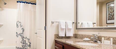 A bathroom with a shower, a sink, a mirror, and a towel rack.