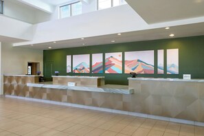 A hotel reception area with a modern design, featuring a reception desk, a green wall with artwork, and a high ceiling with skylights. - Residence Inn by Marriott Phoenix Desert View at Mayo Clinic (Phoenix)