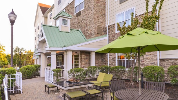 An outdoor patio area with a round table and chairs, a green umbrella, and a stone building in the background.