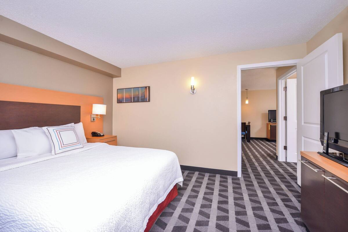 A hotel room with a large bed, a TV, a desk, and a painting on the wall.