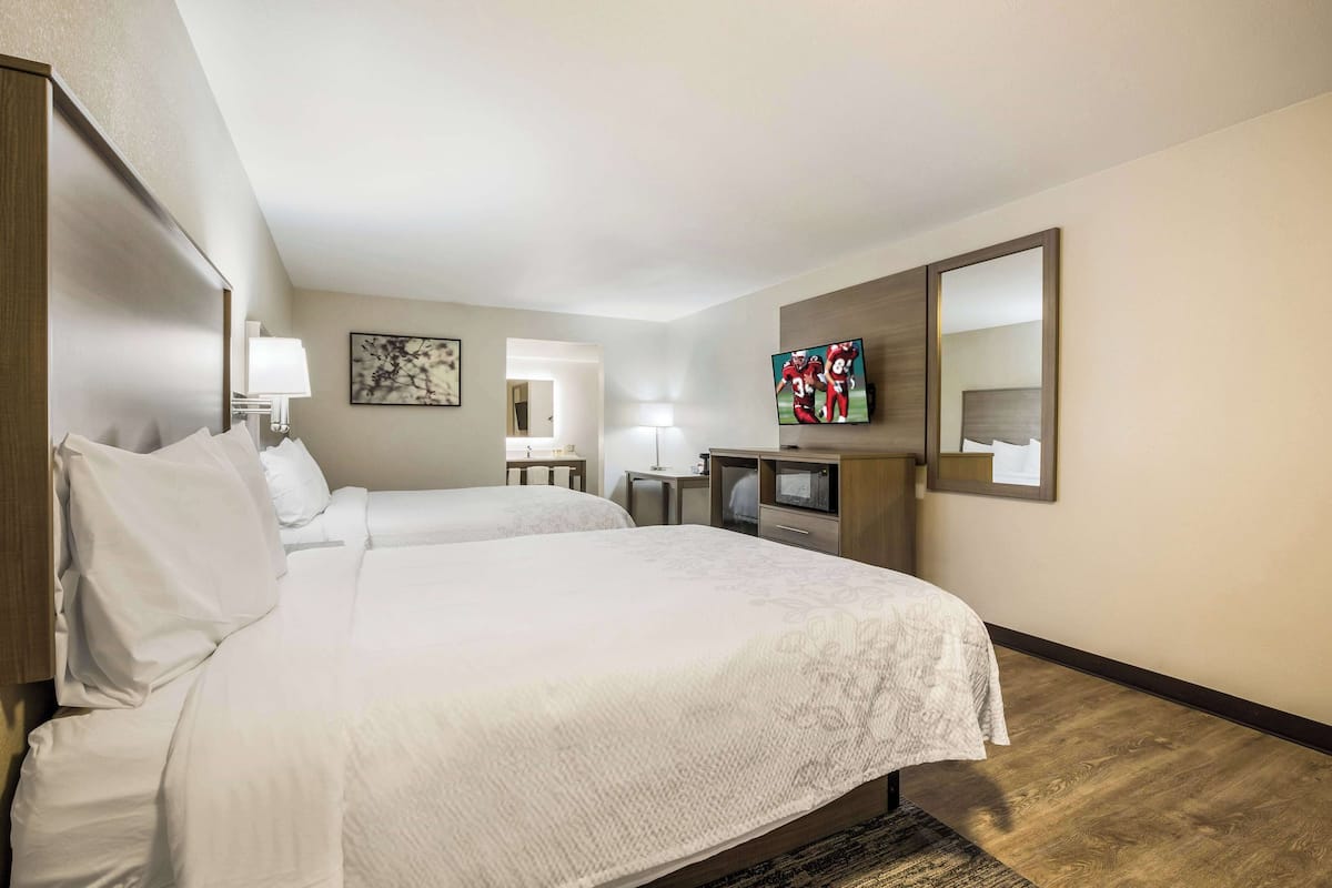 A hotel room with two beds, a TV, a desk, and a mirror.