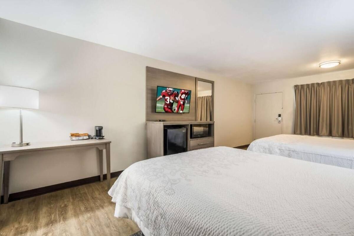 A hotel room with two beds, a desk with a lamp, a television, and a minibar.