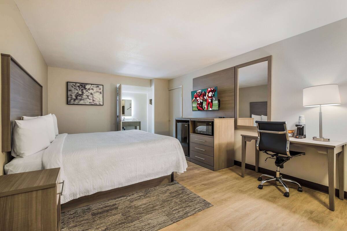 A hotel room with a bed, desk, chair, TV, and a mirror.