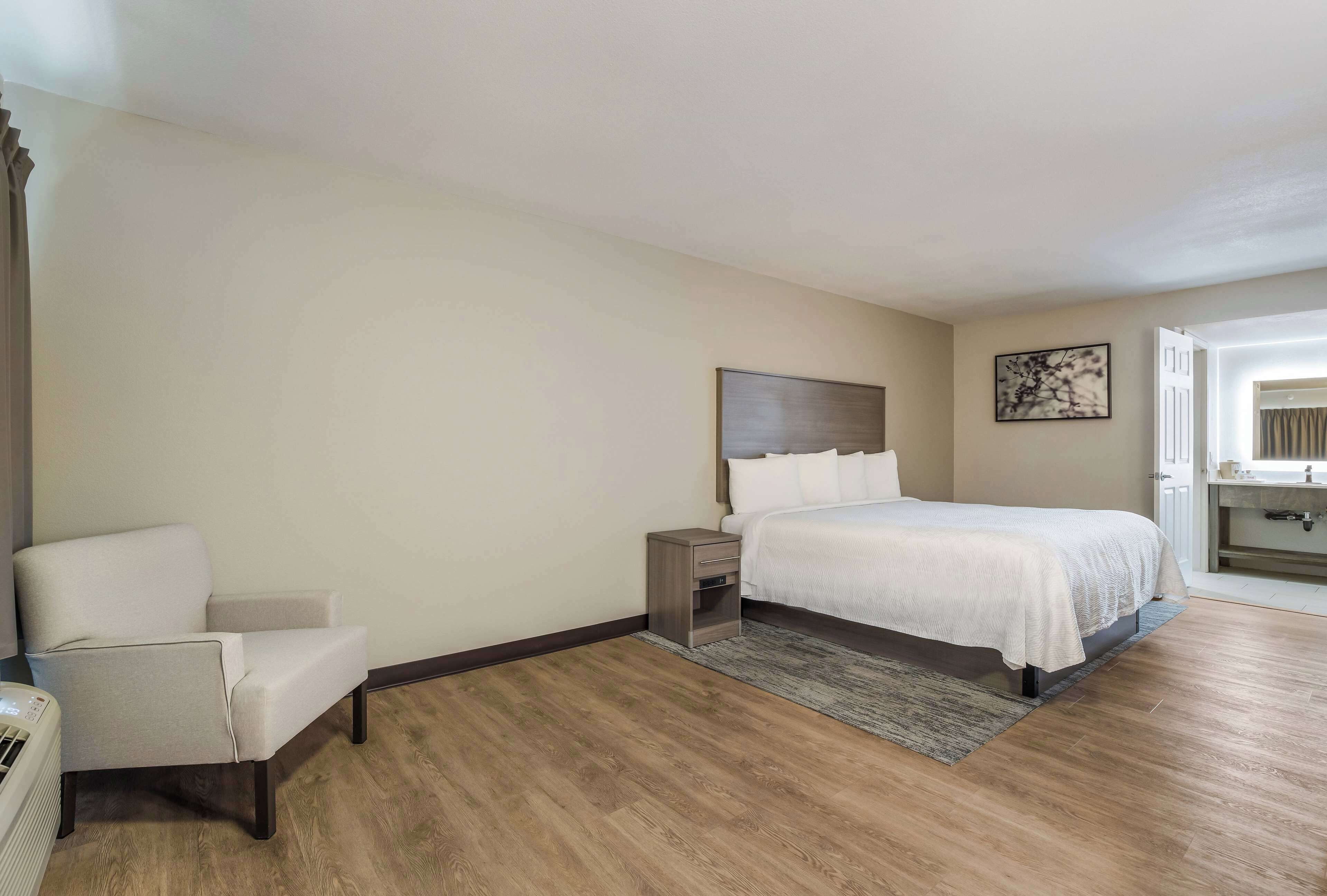 A bedroom with a bed, a chair, a nightstand, and a painting on the wall.