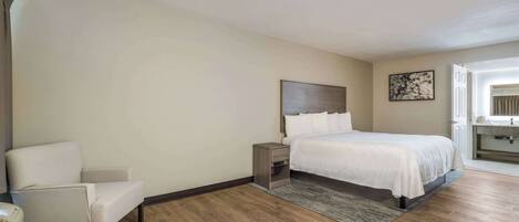 A bedroom with a bed, a chair, a nightstand, and a painting on the wall.