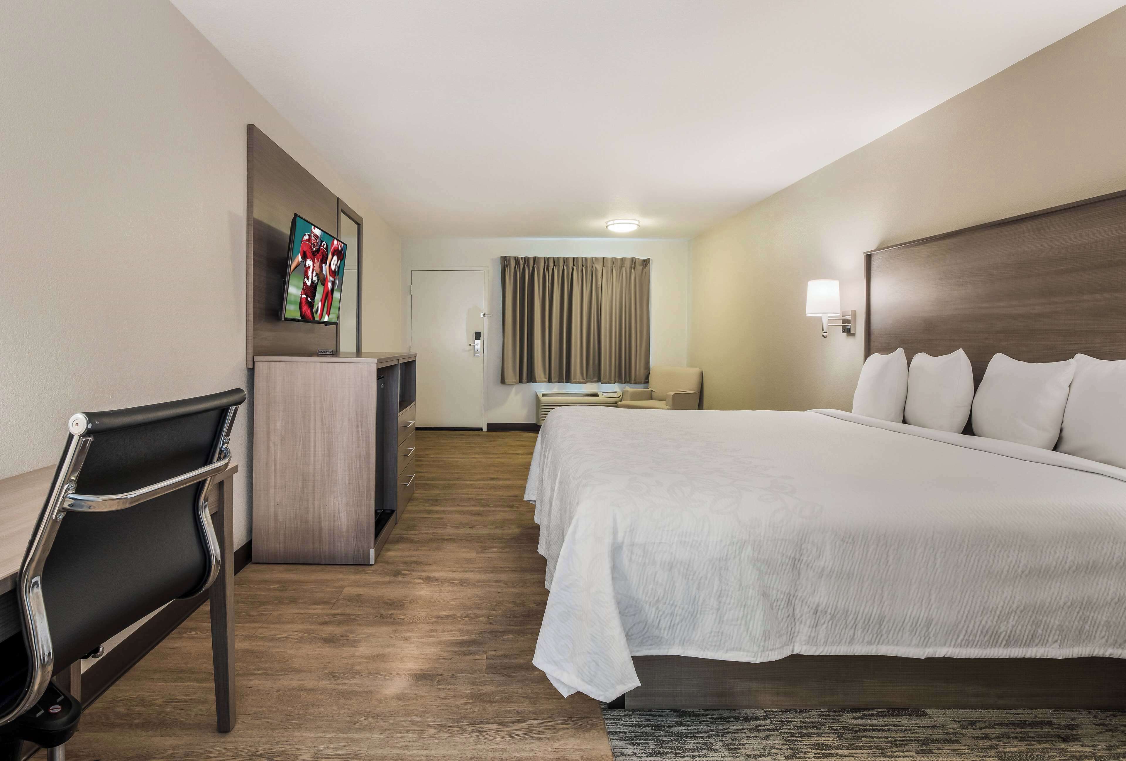 A hotel room with a bed, a desk with a chair, a TV, and a bathroom door.
