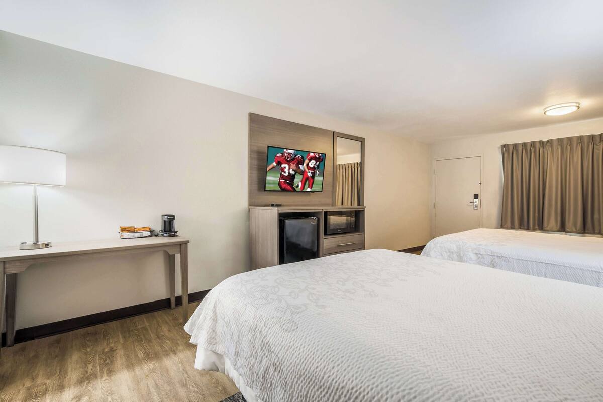 A hotel room with two beds, a desk with a lamp, a TV, and a minibar.