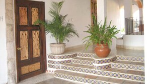 A set of steps leading to a door with intricate woodwork, flanked by potted plants.