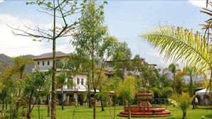 A well-maintained garden with a fountain, surrounded by a variety of trees and a building in the background.