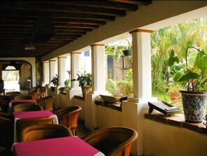 A covered outdoor seating area with wooden chairs and tables, potted plants, and a view of greenery. - Hotel Hacienda La Puerta de Enmedio (Mascota)