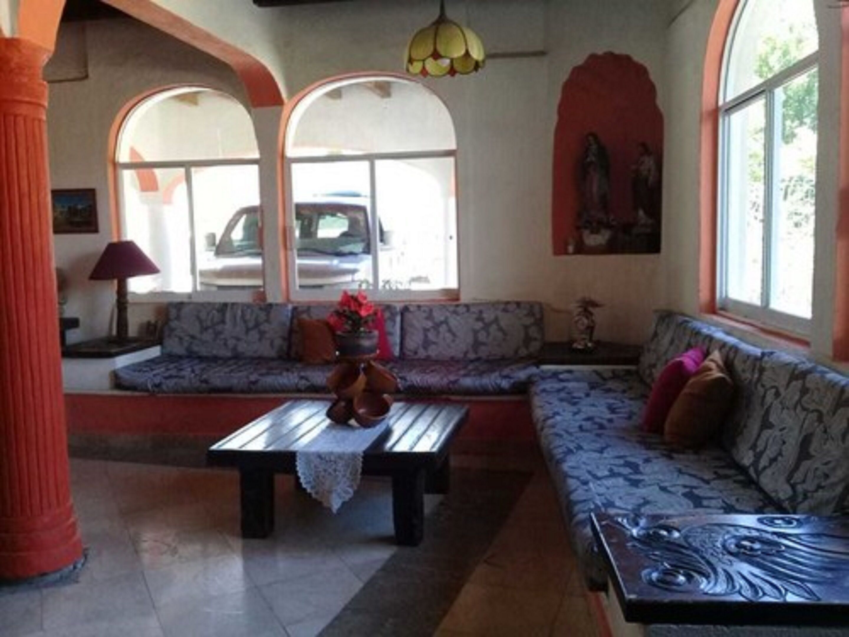 A living room with a sofa, a coffee table, and a lamp. There are windows and a statue on the wall.