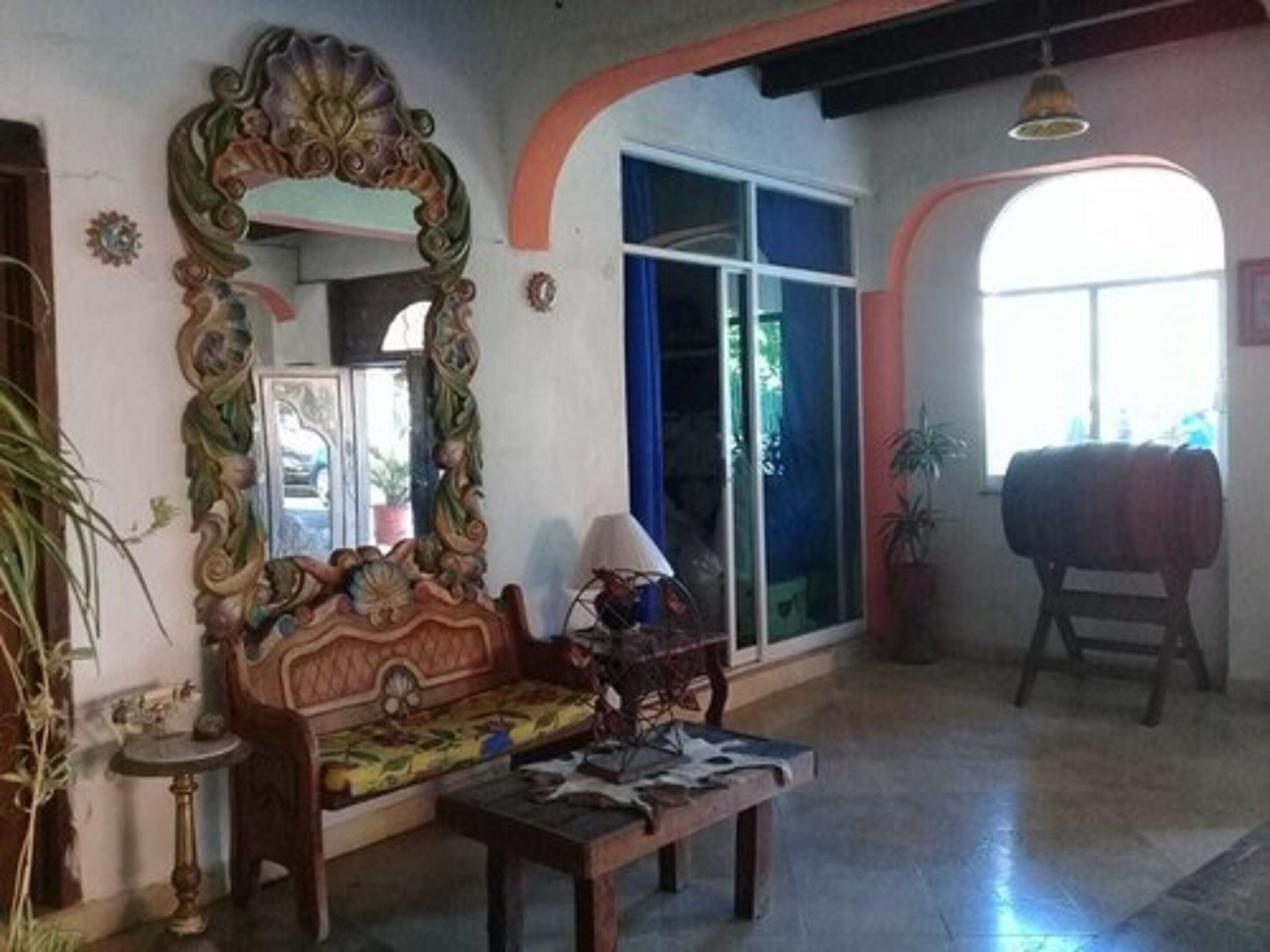 A room with a large ornate mirror, a wooden sofa, a small table, and a window with blue curtains.