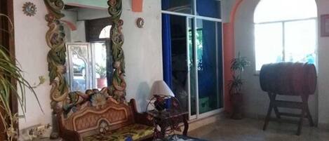 A room with a large ornate mirror, a wooden sofa, a small table, and a window with blue curtains.
