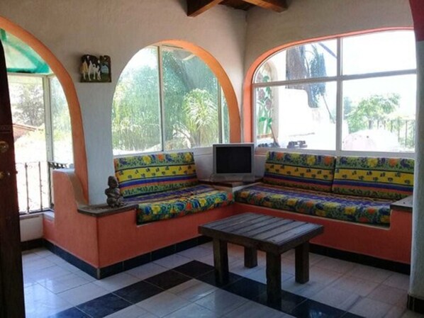 Una habitación con un banco curvo, un televisor y una ventana con vistas a la vegetación.