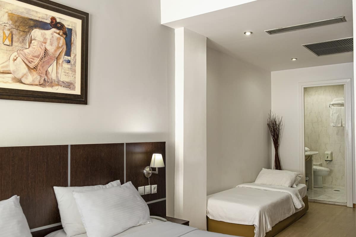 A hotel room with a large bed, a smaller bed, a painting on the wall, and a bathroom visible through an open door.