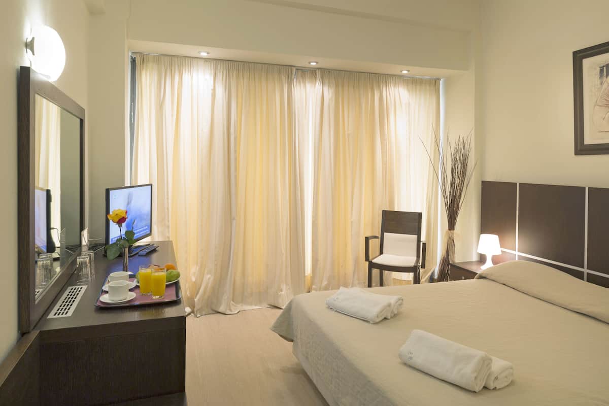 A hotel room with a bed, a desk with a computer, a chair, and a window with curtains.