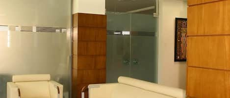 Habitación de hotel moderna con sofá, dos sillones, una mesita de centro y cabina de ducha de vidrio.