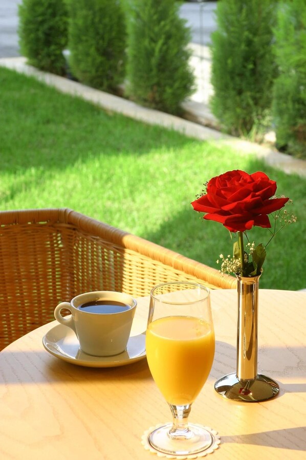 A table with a cup of coffee, a glass of orange juice, and a vase with a red rose.