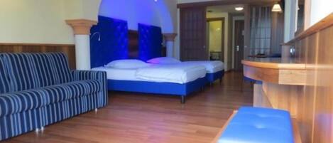 Une chambre d’hôtel avec un lit, un canapé, un banc en bois et un comptoir de réception.