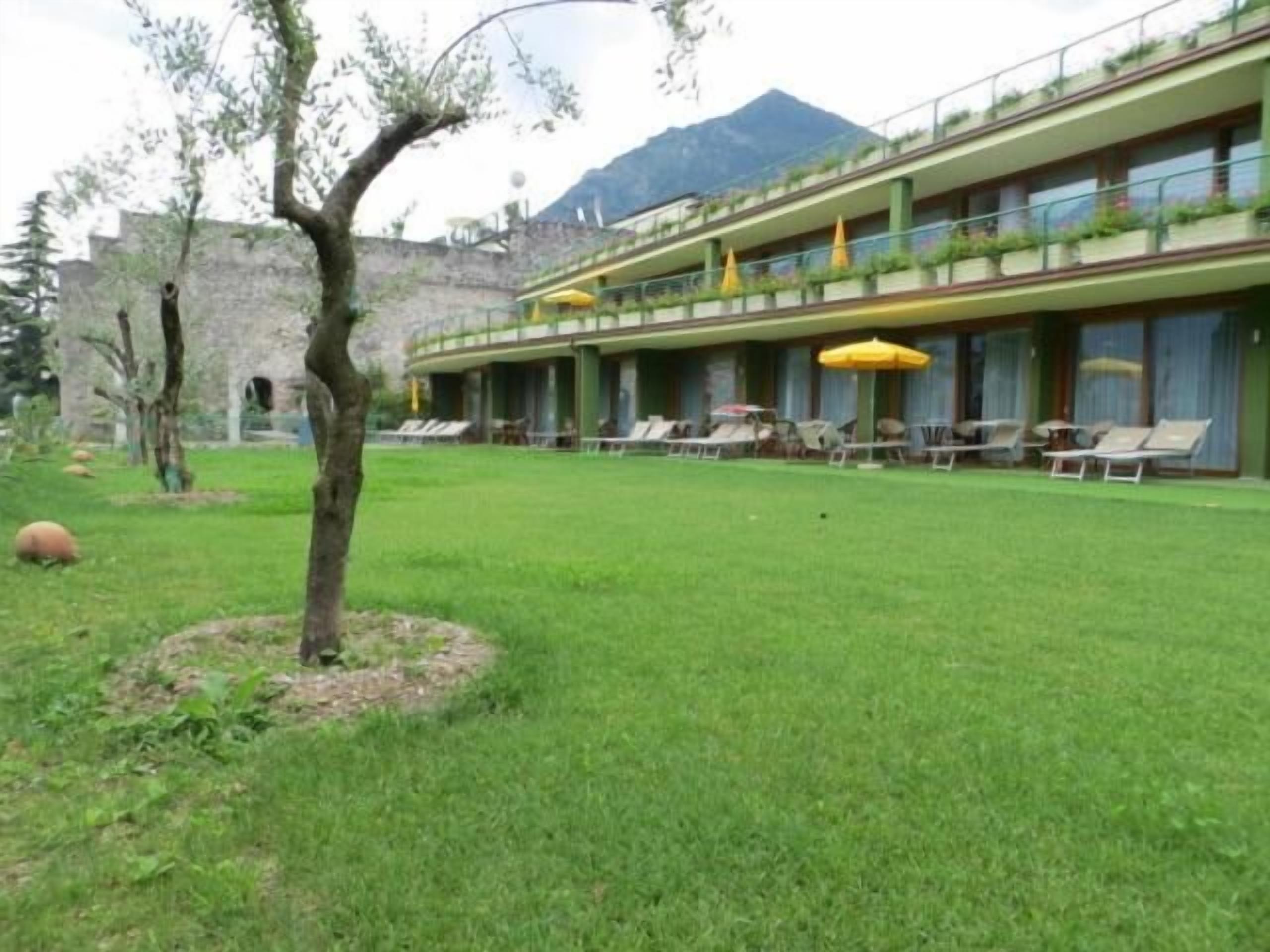 A hotel with a green lawn, outdoor seating with umbrellas, and a mountain backdrop.