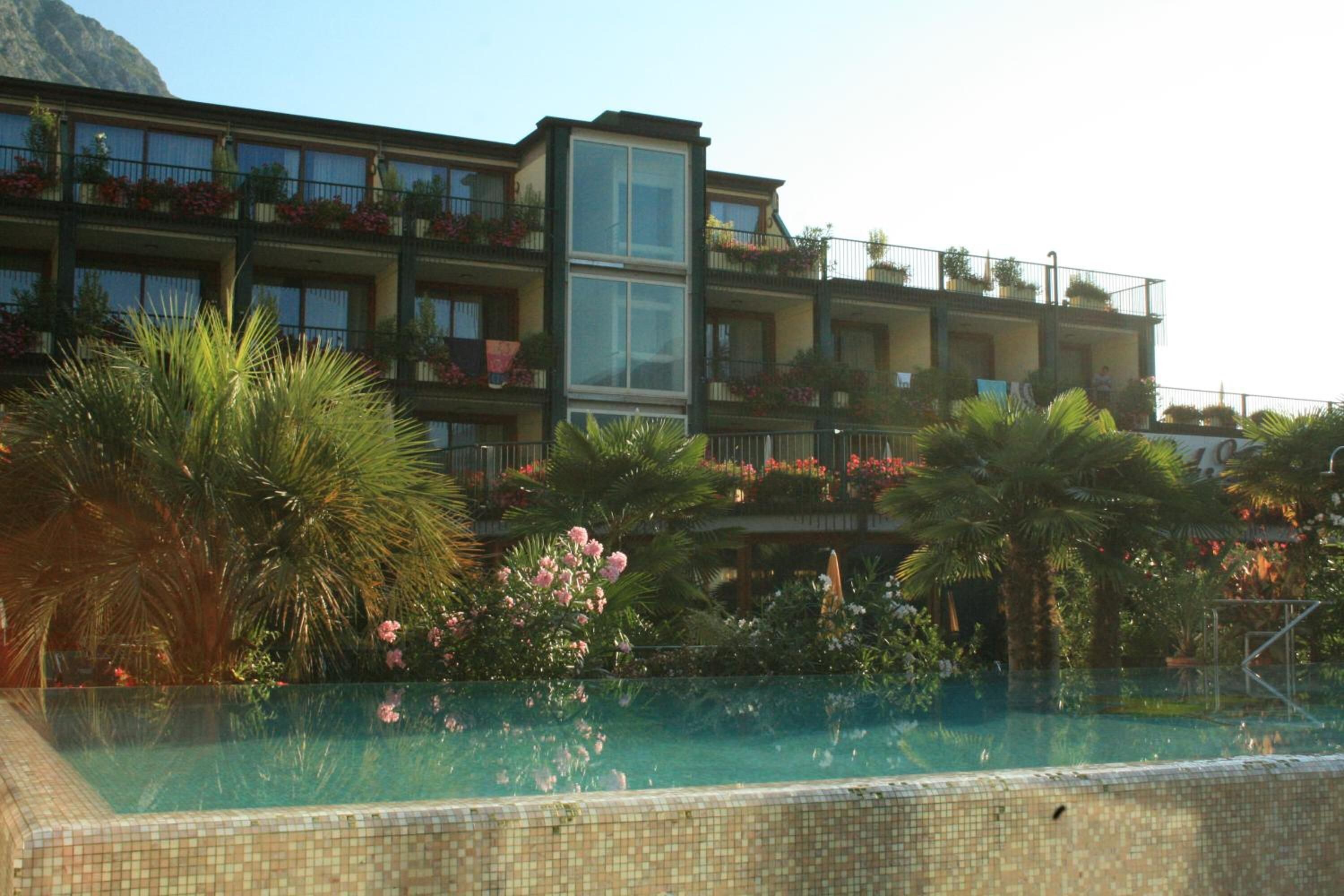 A hotel with a swimming pool, balconies with plants, and a mountainous backdrop.